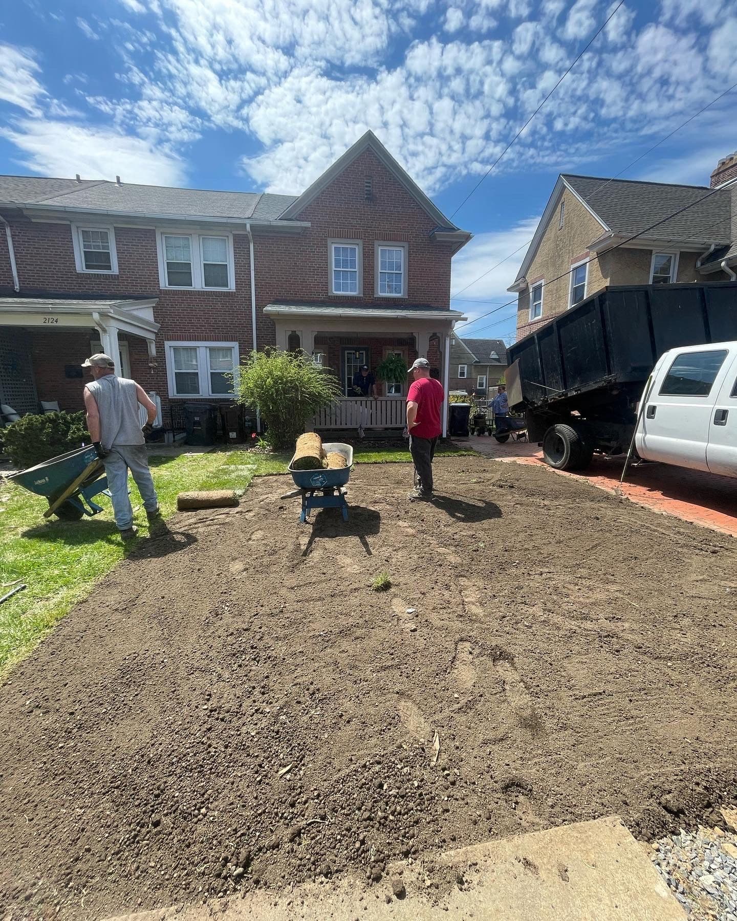 Two Panorama crew members grading a yard with wheelbarrows, dump truck parked on the street